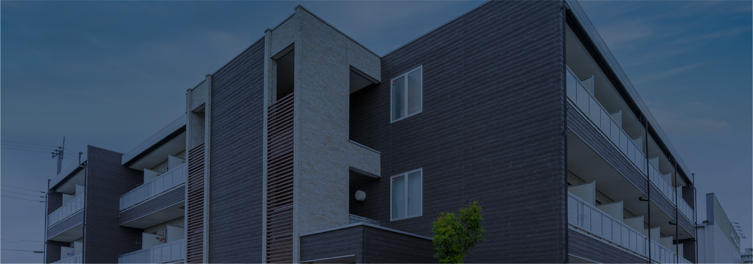 現代的なデザインのマンション外観。複数のバルコニーと窓が見え、建物の外壁は黒とベージュのタイル調で仕上げられている。